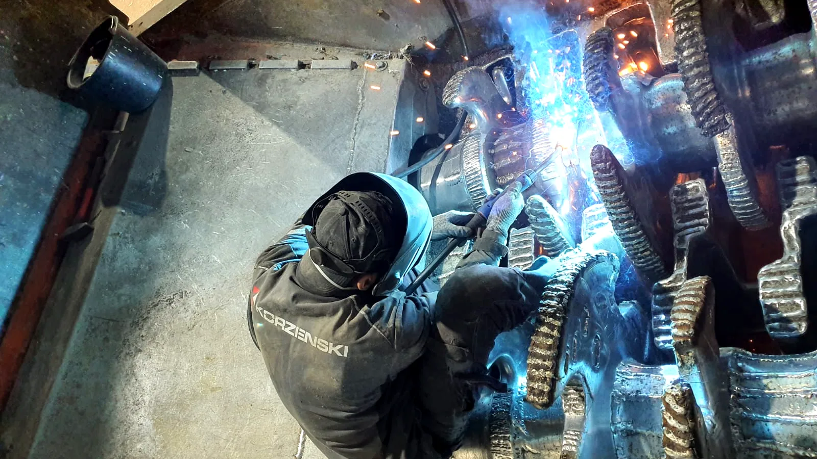 Schweißer der Korzenski Service GmbH panzert die Zahnhalter einer Zerkleinererwelle im Maschinentrichter auf