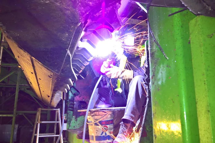 Schweißer arbeitet im Inneren einer Sortier- und Zerkleinerungsanlage, Lichtbogen und Funkenflug